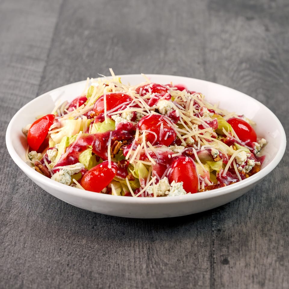 Fresh salad with lettuce, tomatoes, cranberries, blue cheese, pecans, and shredded Parmesan in a white bowl.