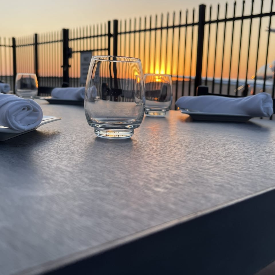 An outdoor dining table set with glasses and napkins overlooking the runway at sunset.
