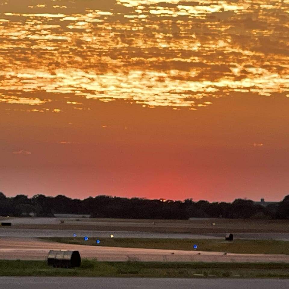 A vivid red and gold sky over the runway at dusk with blue taxiway lights.