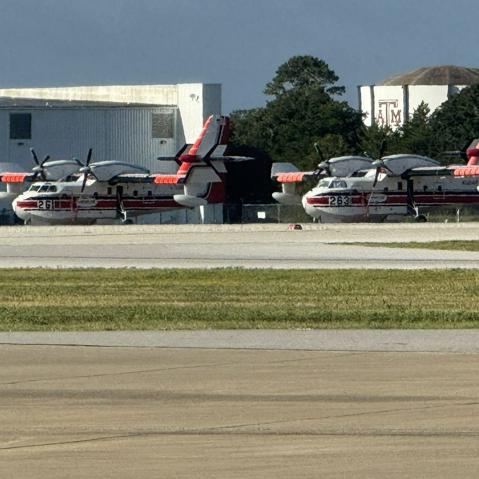 Three red-and-white amphibious aircraft parked beside an airport building and taxiway.