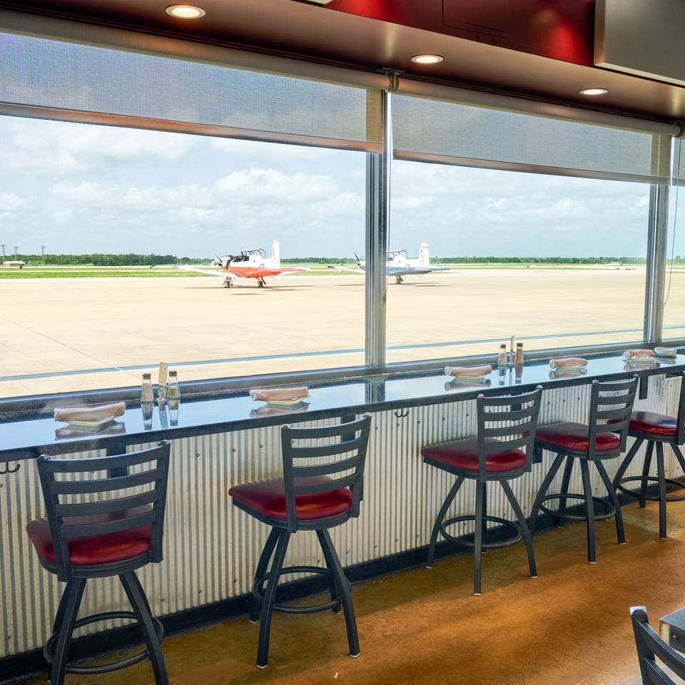 A restaurant counter with bar stools overlooks an airport runway with two small planes.