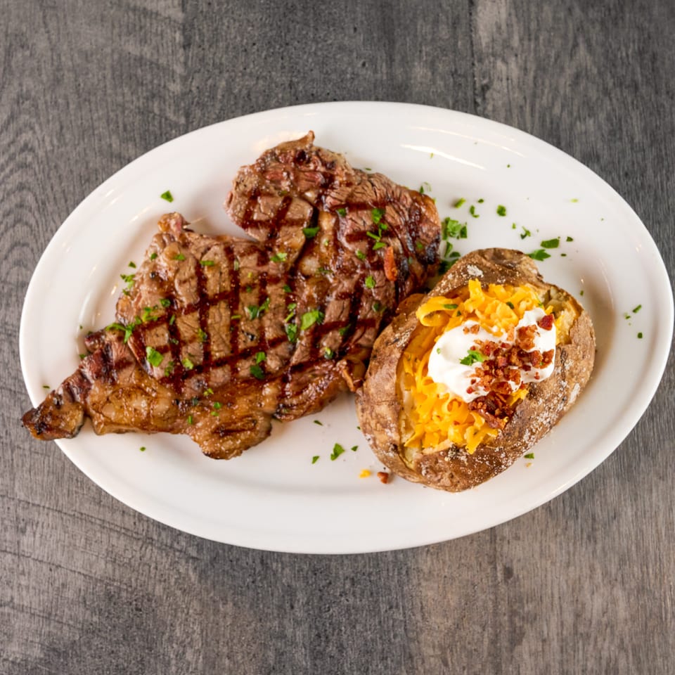 Grilled steak with grill marks and parsley, served with a loaded baked potato on a white plate.