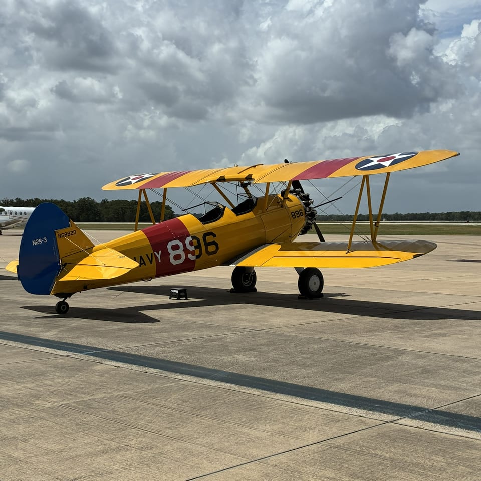Yellow and red vintage biplane parked on an airport runway beneath dramatic clouds.