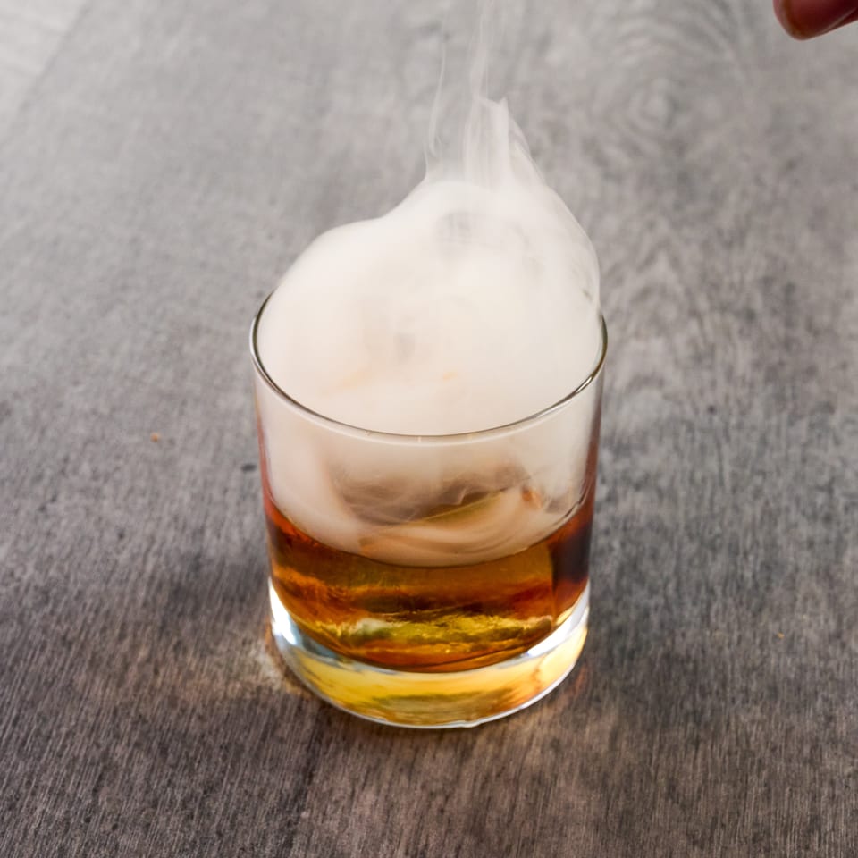Smoked whiskey cocktail in a rocks glass, with white smoke swirling above the amber liquid.