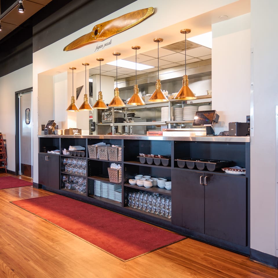 Restaurant kitchen pass-through with copper pendant lights, a wooden propeller decoration, and organized dishware.