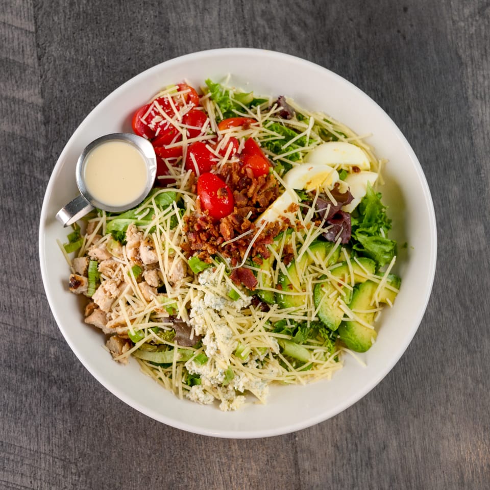 Overhead view of a Cobb salad with chicken, bacon, avocado, egg, tomatoes, and dressing.