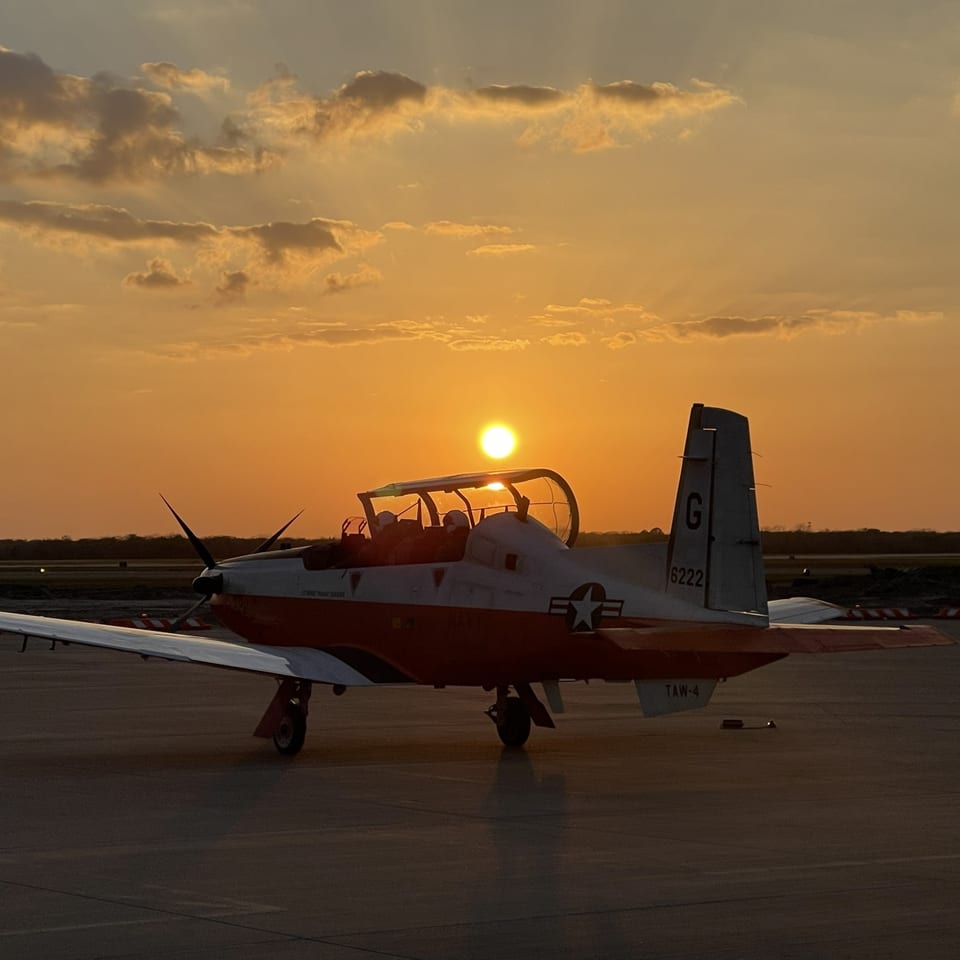 A T-6 training aircraft with pilots aboard, the sun setting directly behind the canopy.
