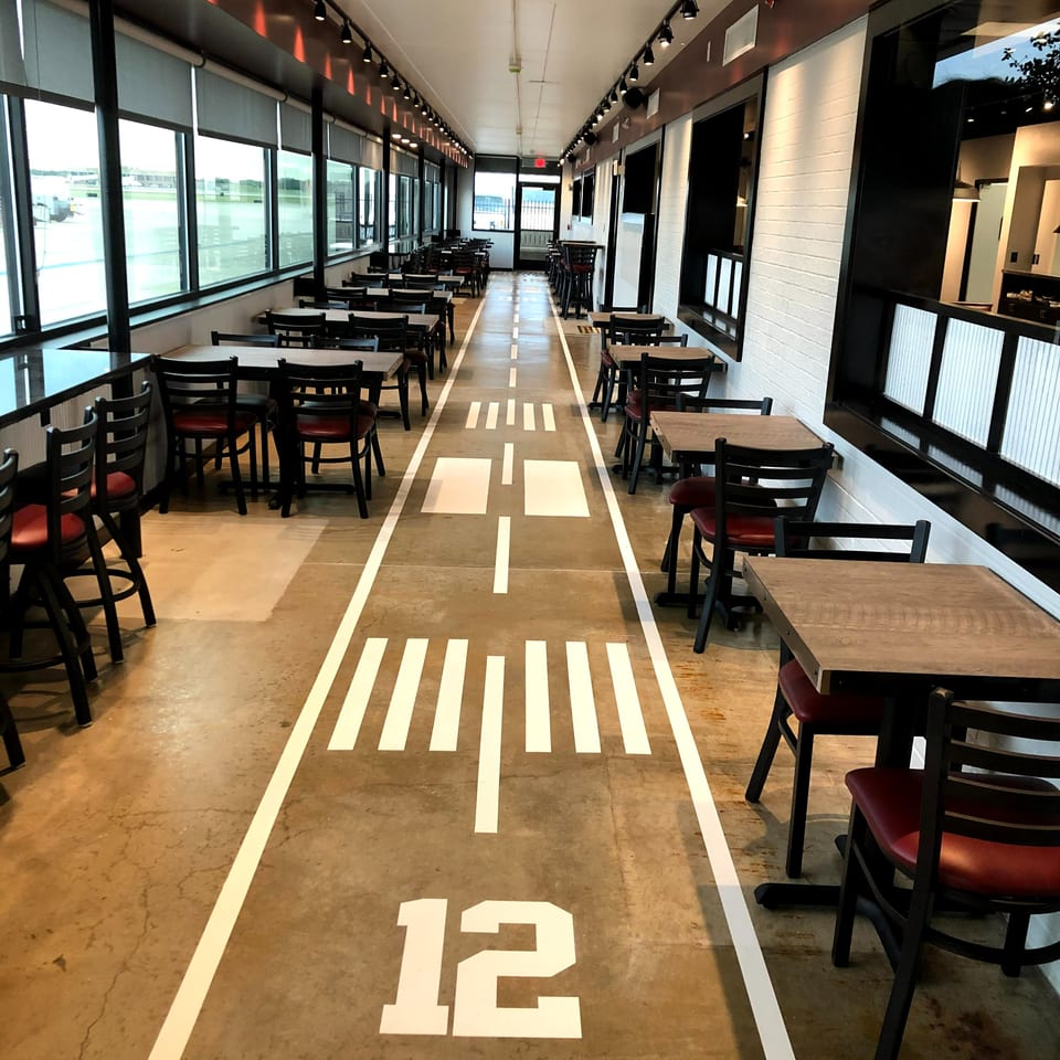 Spacious restaurant dining area with rows of tables, large windows, track lighting, and a road-themed floor design.