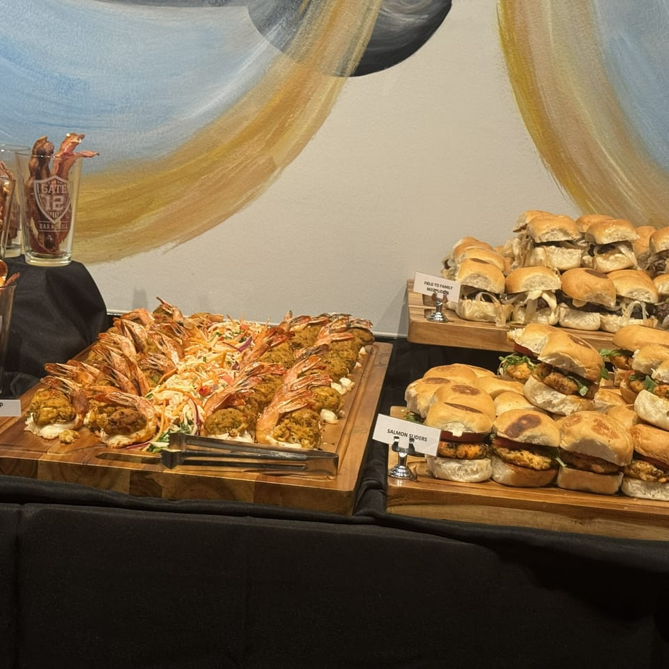 Buffet display featuring stuffed shrimp, skewered appetizers, and trays of salmon sliders and other sandwiches.
