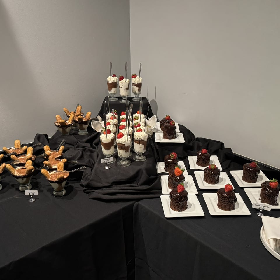 Dessert buffet featuring chocolate mousse, tiramisu, chocolate ganache cakes, whipped cream, and strawberries on black-draped tables.