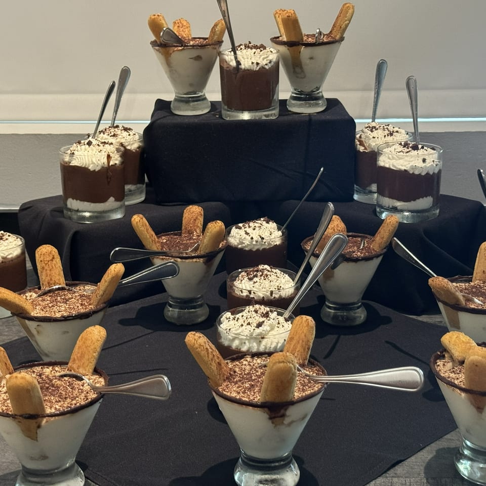 Display of layered chocolate mousse desserts topped with whipped cream, chocolate shavings, and cookies in individual glasses.
