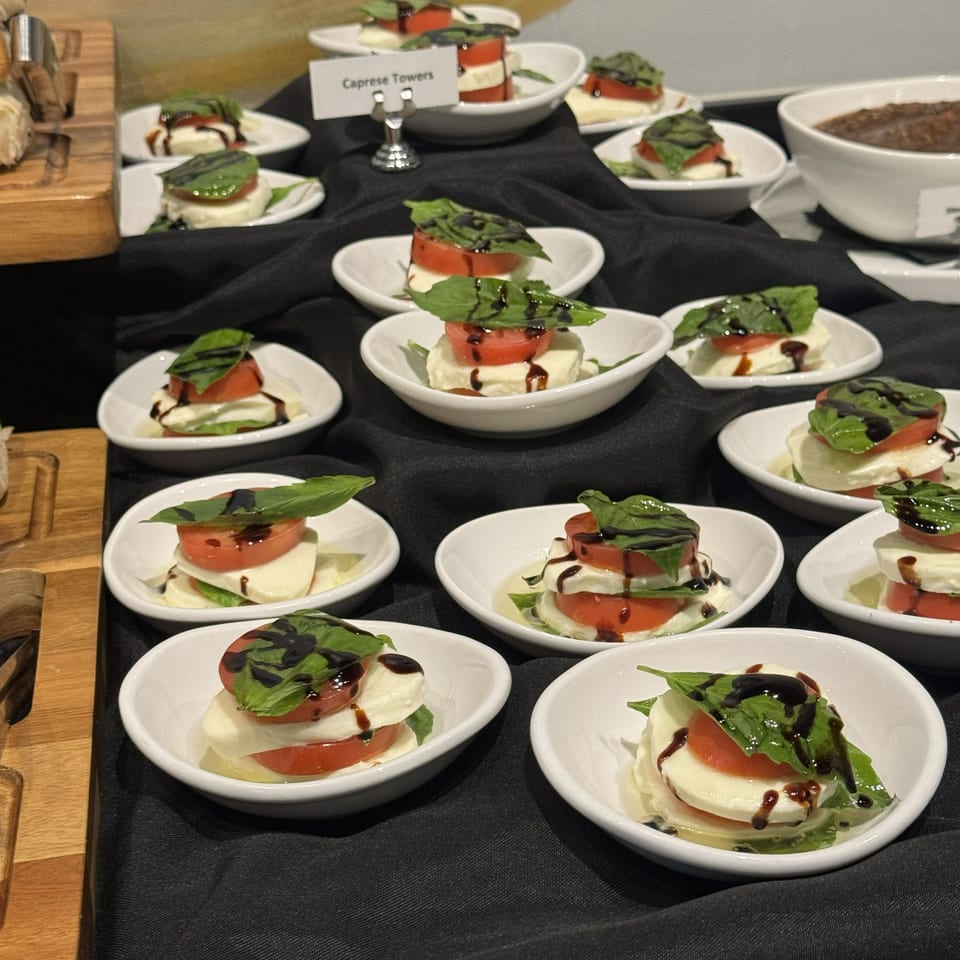 Numerous plates of Caprese salad stack tomatoes, mozzarella, and basil, drizzled with balsamic glaze on a buffet table.