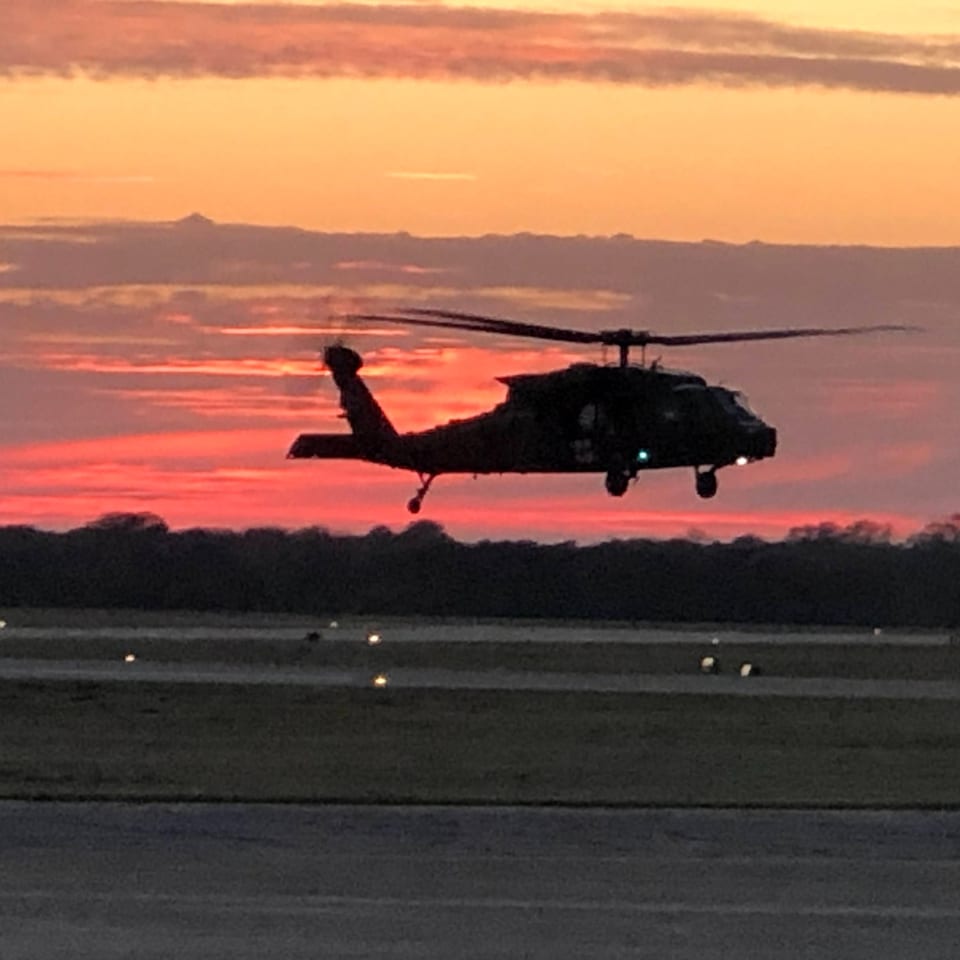 A helicopter flying low over the runway against a pink and orange sunset.