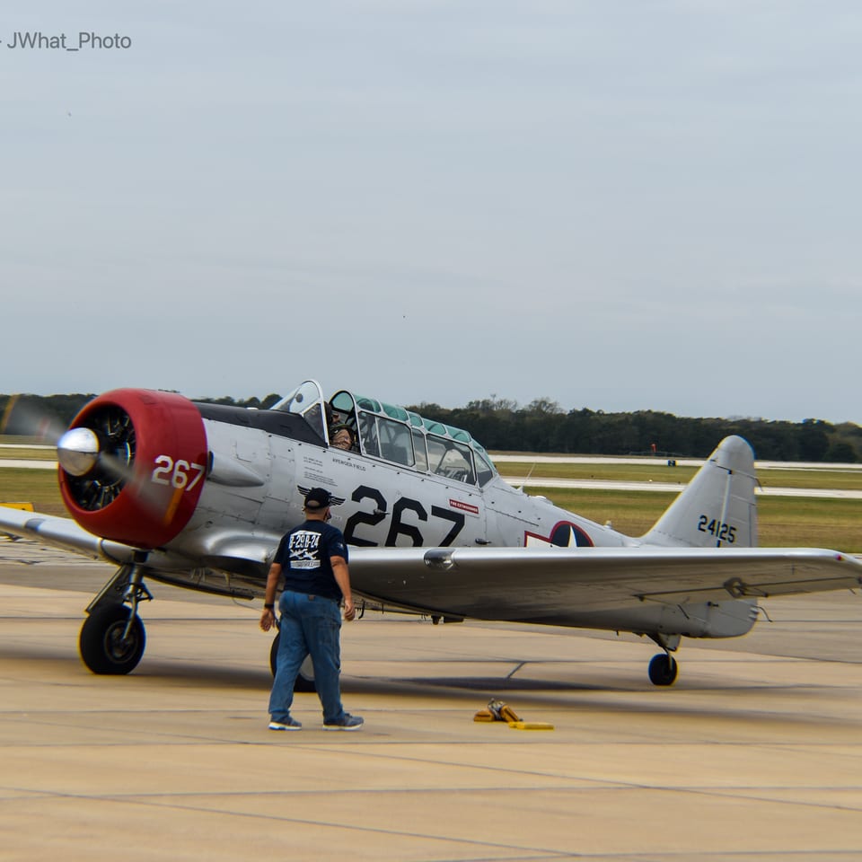 Vintage silver and red propeller aircraft parked on an airport tarmac, with a person standing beside it.
