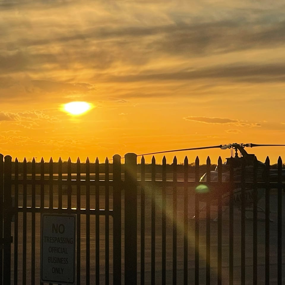 Golden sunset over a fenced industrial waterfront, with silhouetted utility equipment and a no-trespassing sign.