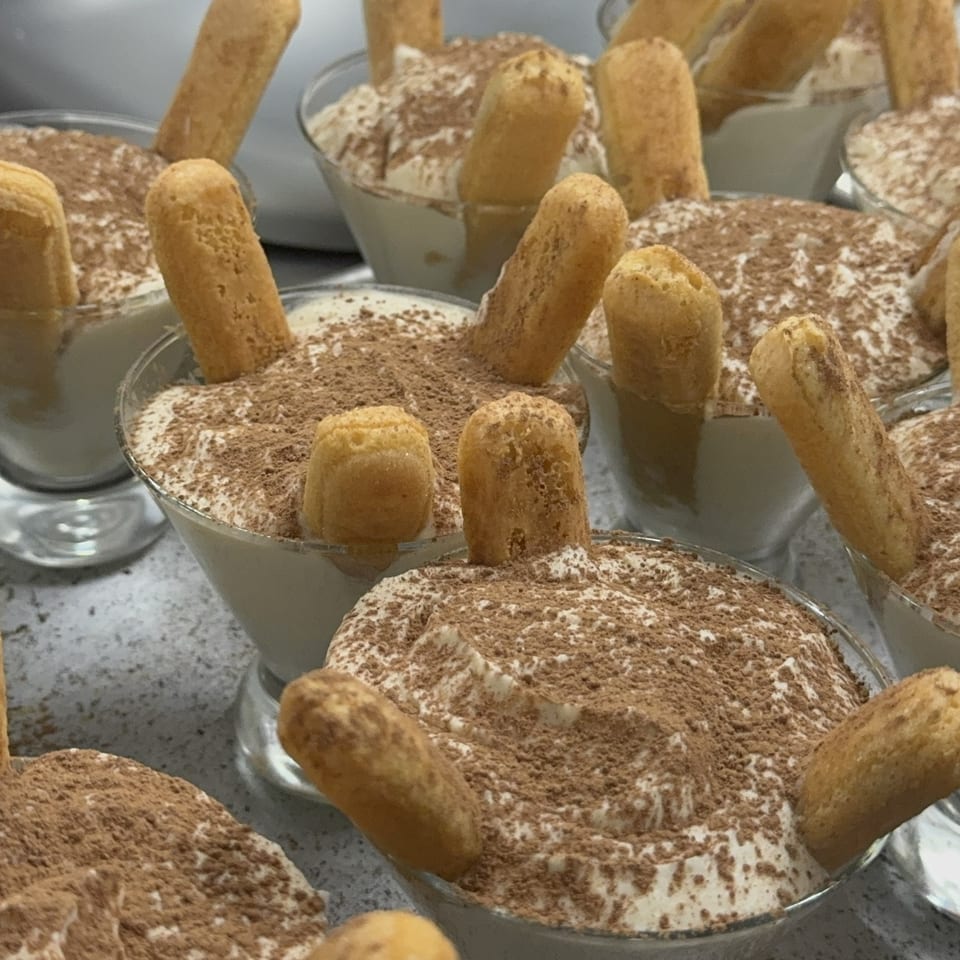 Multiple glasses of tiramisu dusted with cocoa and garnished with upright ladyfinger biscuits.