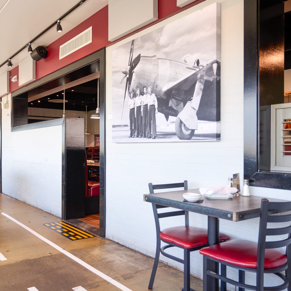Restaurant interior with red and white walls, black tables, red chairs, and a large airplane mural.