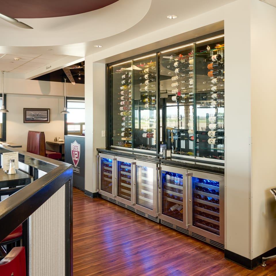 Restaurant interior with a large wine display, bar seating, and dining tables with red booths.